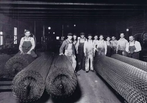 Contractors standing behind giant rolls of chain wire mesh, some of the first chain-link fencing produced in Central Illinois