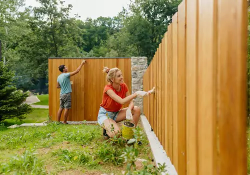 Homeowners painting their fence to show proper Fence Etiquette Between Neighbors